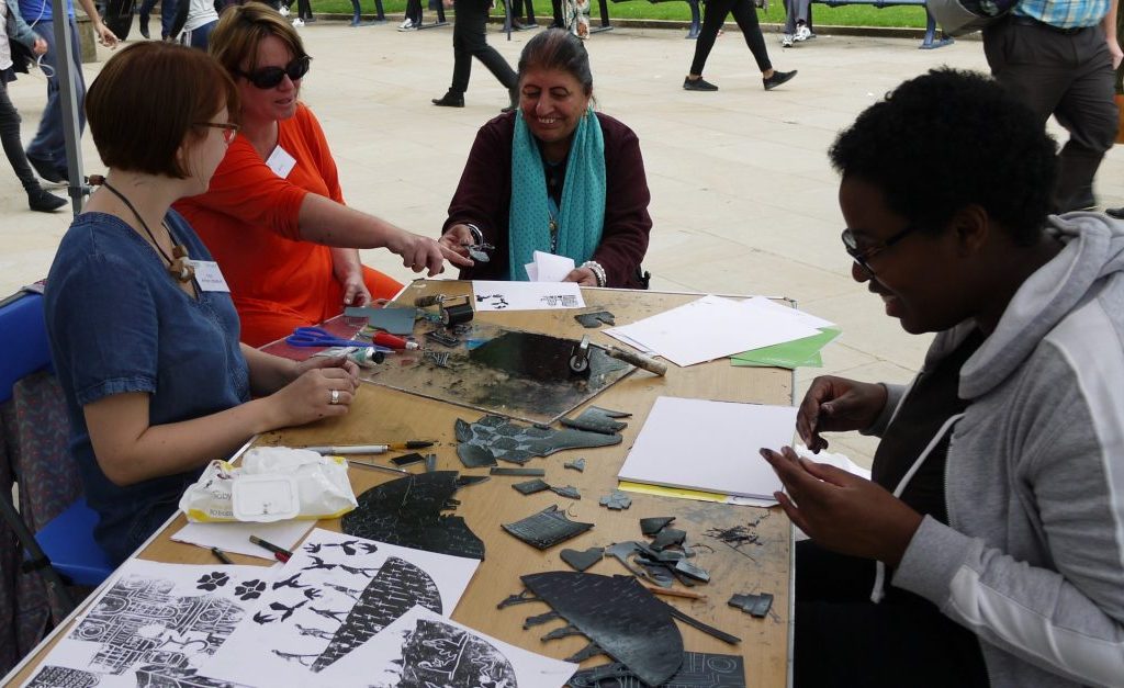 P1070879 Three women interact and talk to the artist around a table whilst linoprinting.