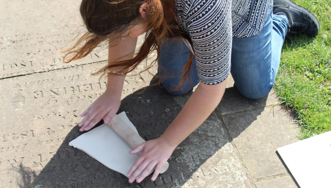 an artist rolls a slab of clay over a gravestone set in the path.
