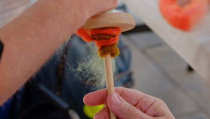 Passerby is spinning a length of wool with a drop spindle