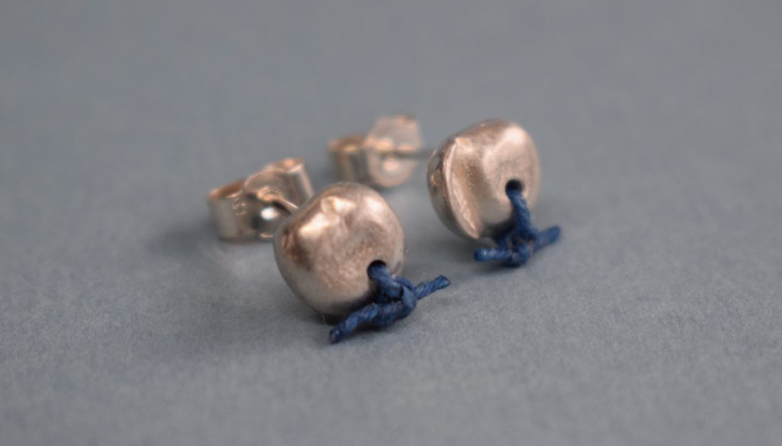 silver earrings with a hole in the stud through which a blue thread was knotted.