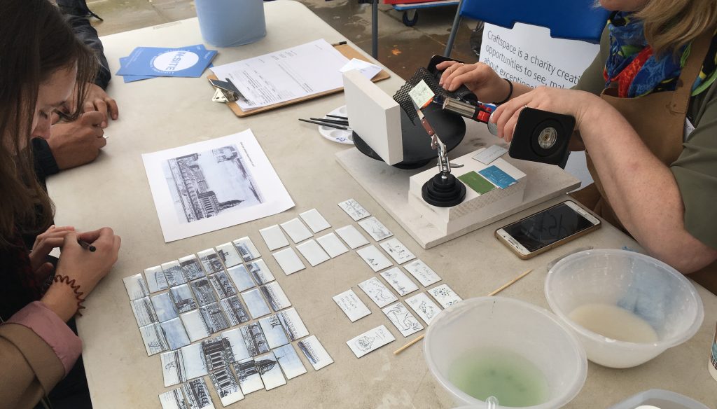 A woman is drawing and the artist is heating the enamel tile.