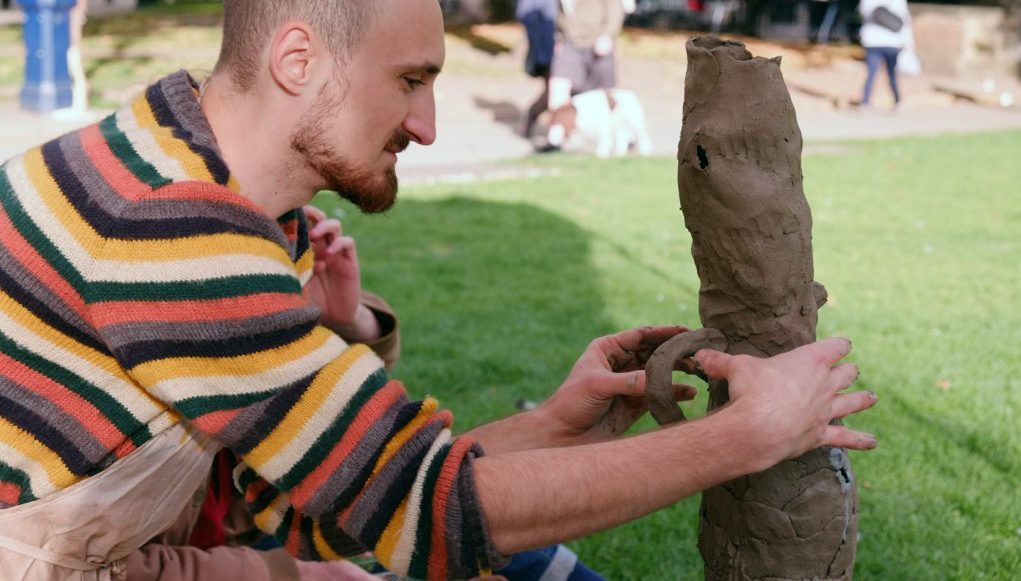 The artist is shaping a tall sculpture with his hands.