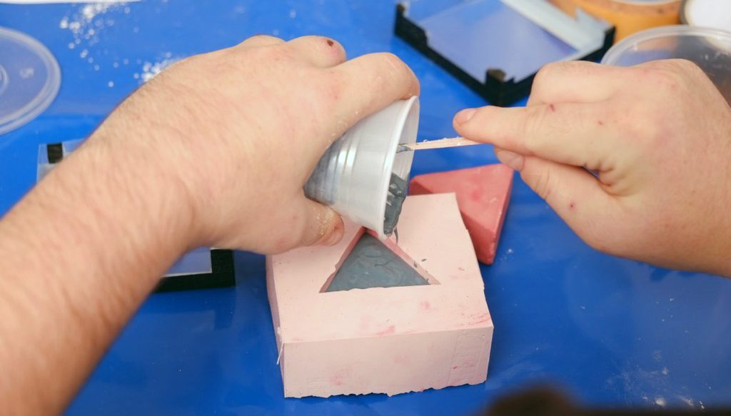 the artist is filling the plaster into a 3D triangle molds.