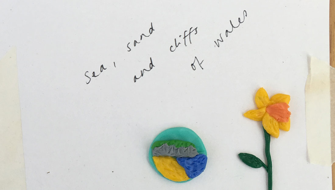 'sea, sand and cliffs of wales' with small beach scene and a daffodil made from modelling clay