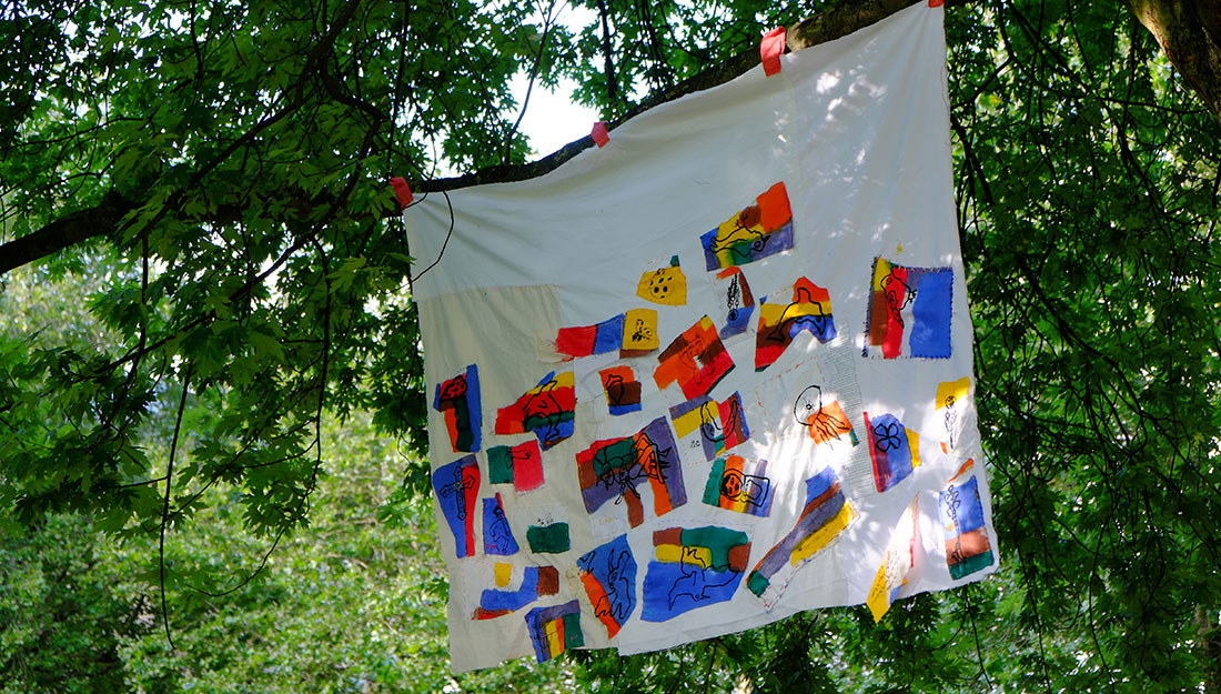 white sheet with colourful applique motifs sewn onto it hanging from a tree